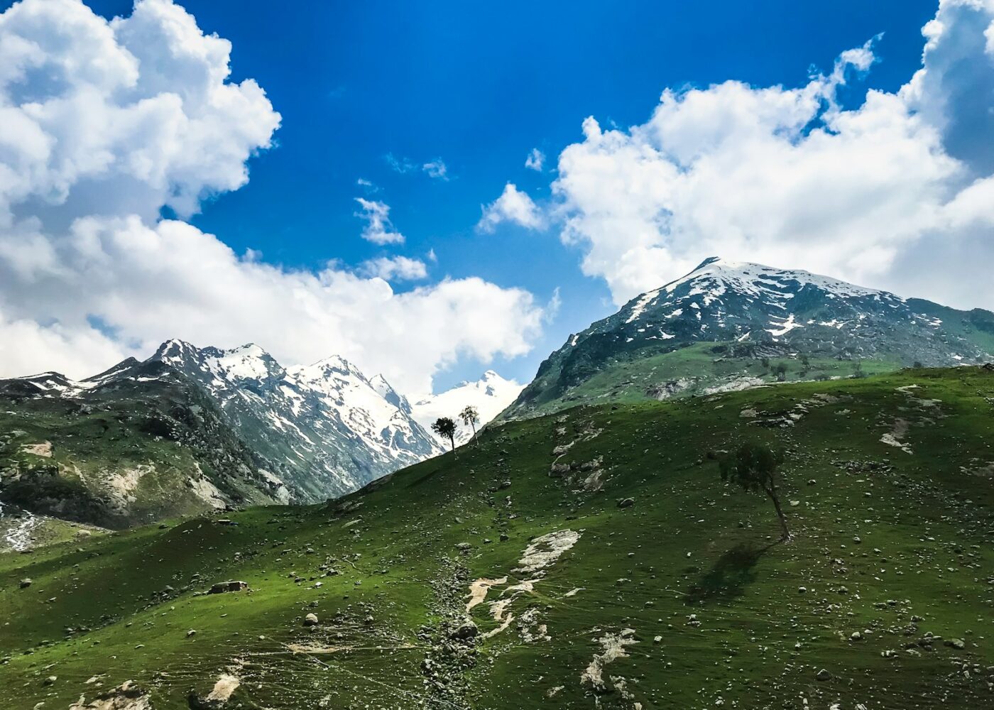 green grass field near snow covered mountain under blue sky during daytime